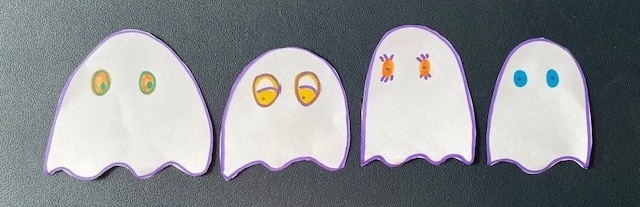 Handmade ghosts cut out of paper with eyes in different colours and expressions.