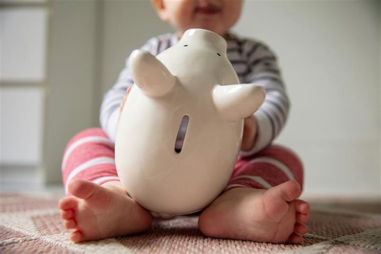 A baby wearing pink and white stripes, holding a white piggy bank