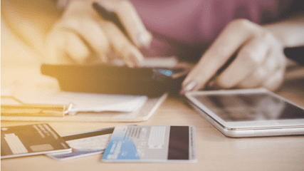 Person using a calculator, phone and credit card to work on their finances