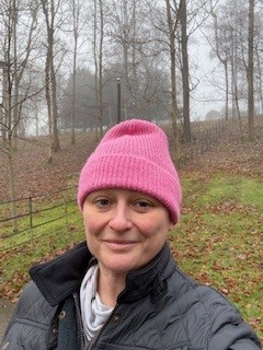 MSE Jenny H on a walk wearing a bright pink beanie hat. The background is an autumnal forest style walk in the Cotswolds