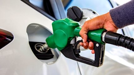 Close up photo of a man's hand holding a green fuel pump in the fuel tank of a white car.