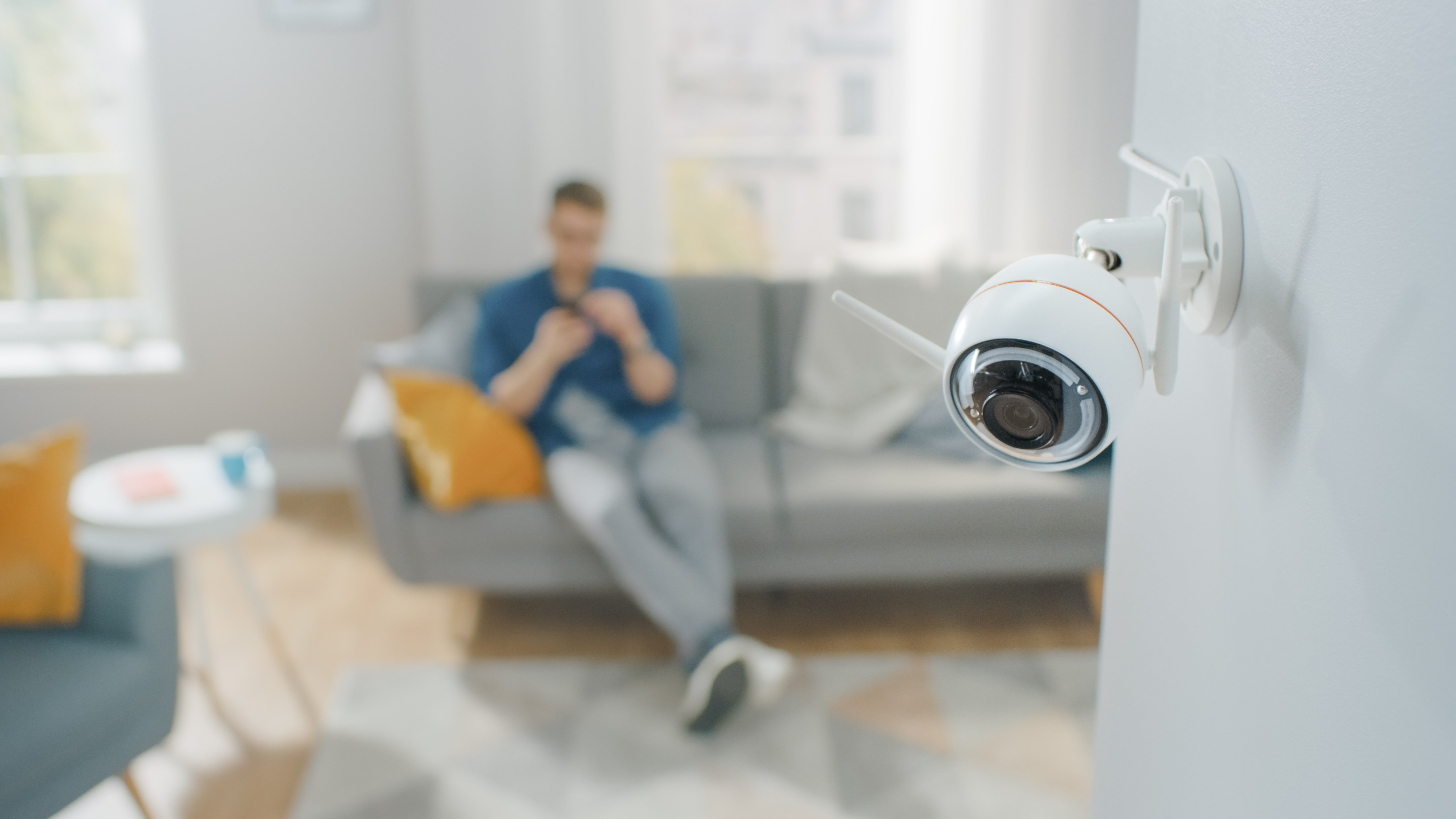 A home security camera with a man in the background sitting on the sofa
