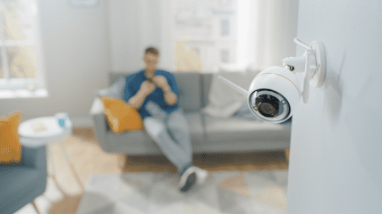 A home security camera with a man in the background sitting on the sofa
