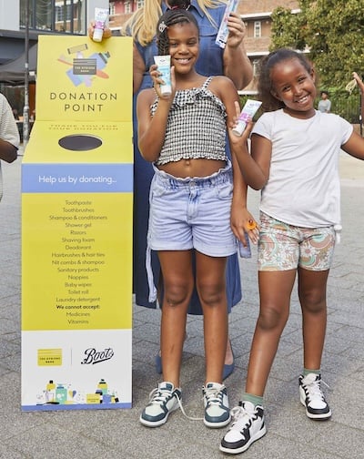 Two girls standing beside a yellow Hygiene Bank donation point, outside