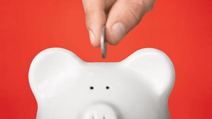 Hand putting a coin into a piggy bank