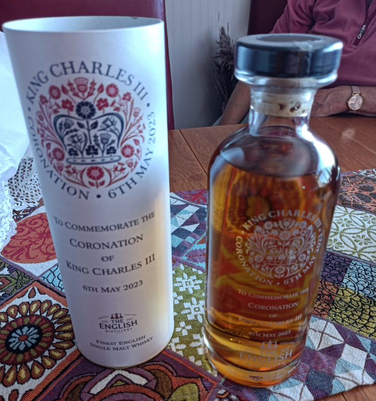 A bottle of Coronation whisky standing next to its white cylinder container