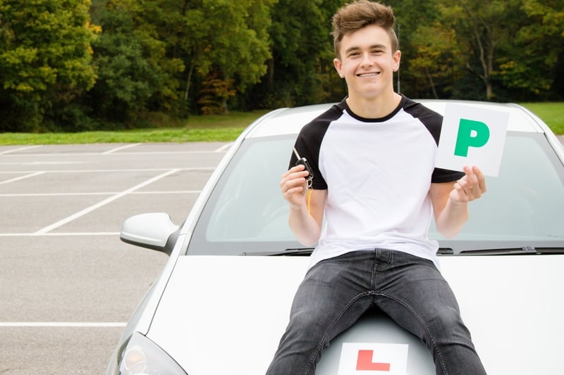A young motorist sat on the bonnet of a car holding a P plate and a car key, with an L plate visible on the car.