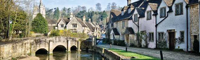 Photo of several houses, a church, a bridge and a river in a picturesque village.
