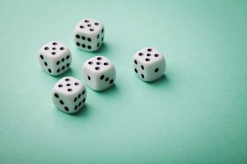 A set of five black and white dice against a green table