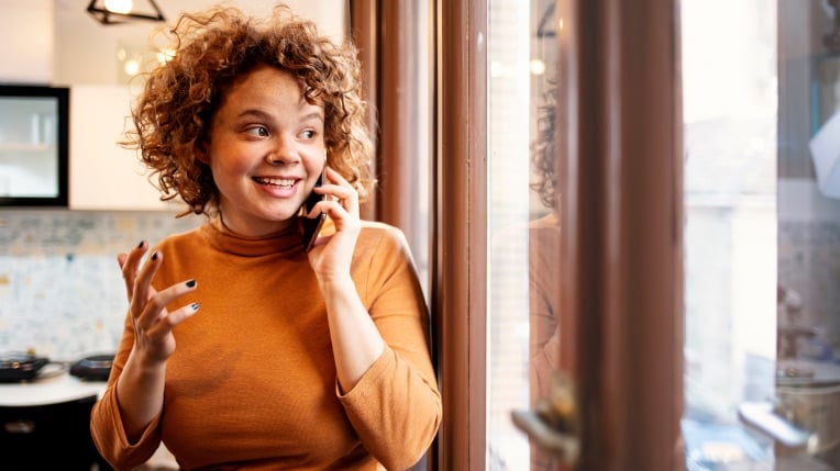 Woman smiling while talking on the phone and looking out of a window.