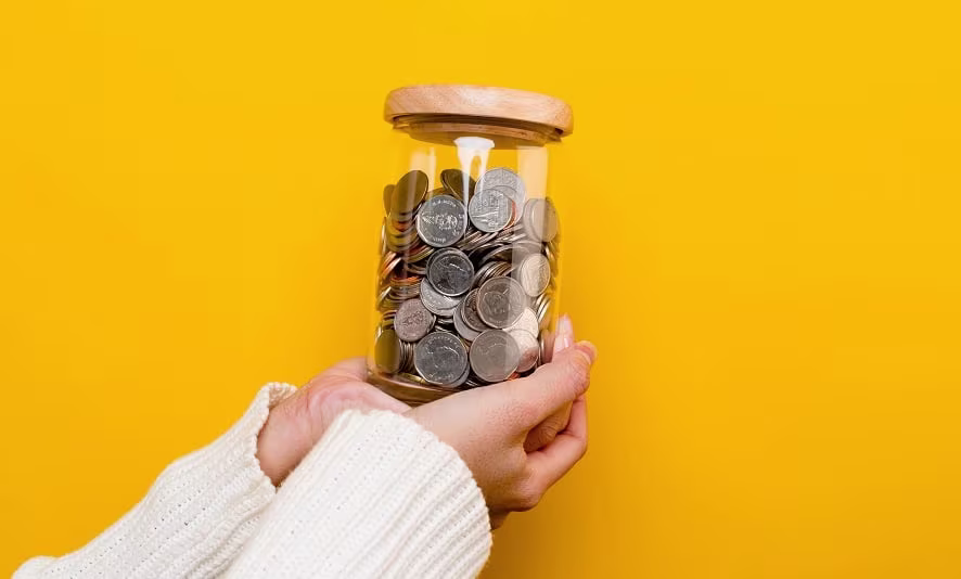 A child's hands putting coins into a piggy bank
