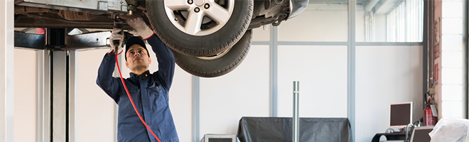 Photo of a male mechanic working beneath a car that has been raised up.