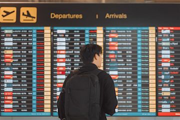 A traveller with a backpack standing in front of a large airport arrivals and departures dashboard