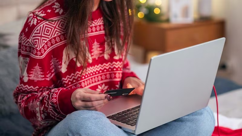 Woman in a Christmas jumper on her laptop holding a credit card.