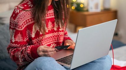 Woman in a Christmas jumper on her laptop holding a credit card.