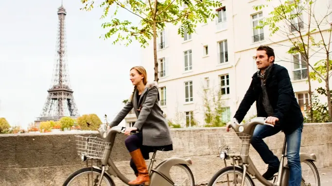 Een man en vrouw fietsen door Parijs met de Eiffeltoren op de achtergrond