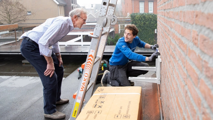 Installateur van warmtepomp met oudere man als klant die toekijkt