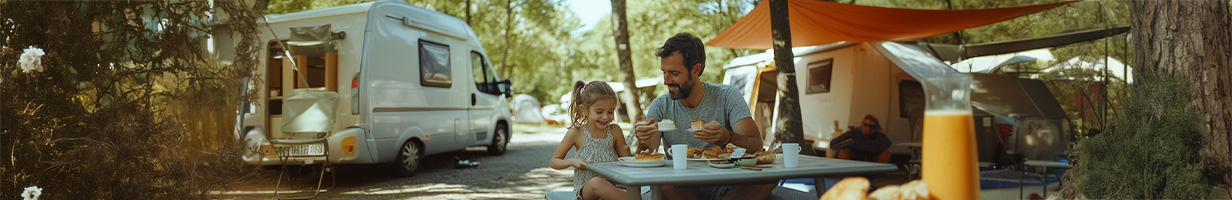 Père et sa fille prennent leur petit déjeuner en pleine nature, devant des caravanes.