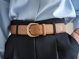 Ceinture en cuir beige avec boucle dorée sur pantalon noir.