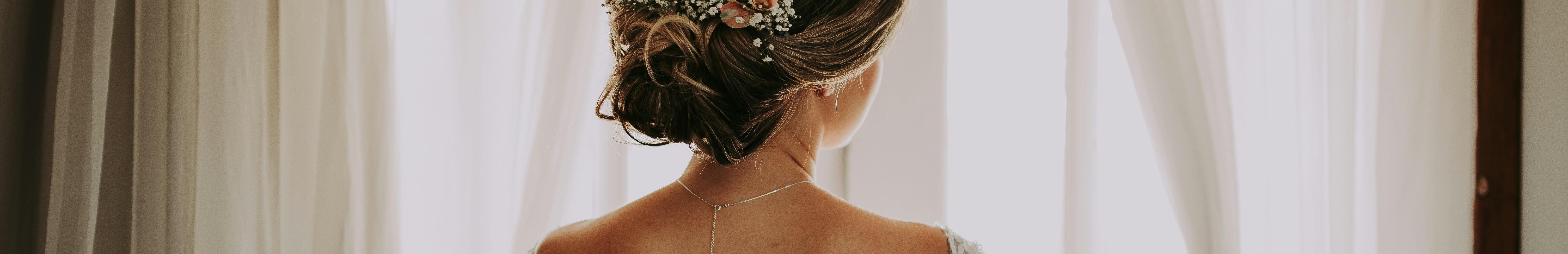 Mariée vue de dos, regardant par la fenêtre, portant sa robe de mariage.