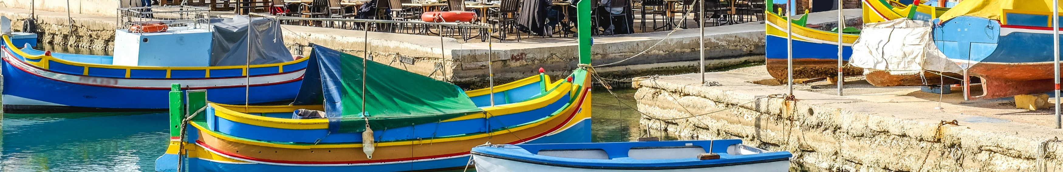 Bateaux colorés amarrés dans une marina à Malte, avec l’eau calme reflétant les couleurs vives des embarcations.
