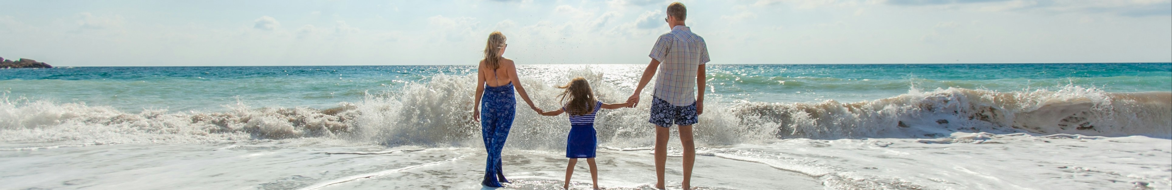 Famille de trois les pieds dans l'eau face à la mer.