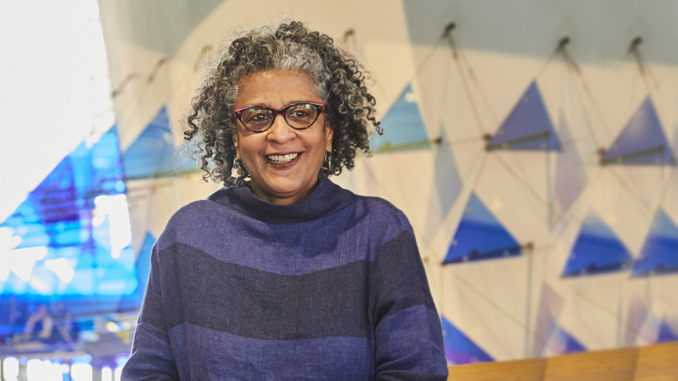 Woman with curly hair and glasses in front of abstract blue glass shapes. 