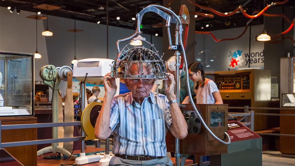 An adult sits underneath the psychograph machine in the Weighing the Evidence exhibit