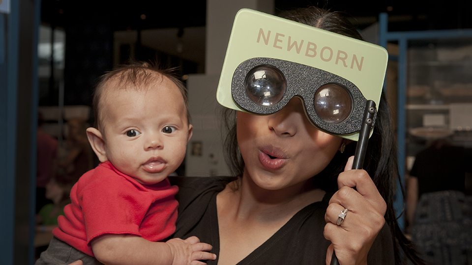 An adult holding up glasses that say "Newborn" while also holding a baby