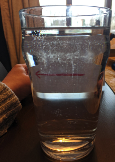 A glass of water in front of a piece of paper with an arrow point to the viewer's left 