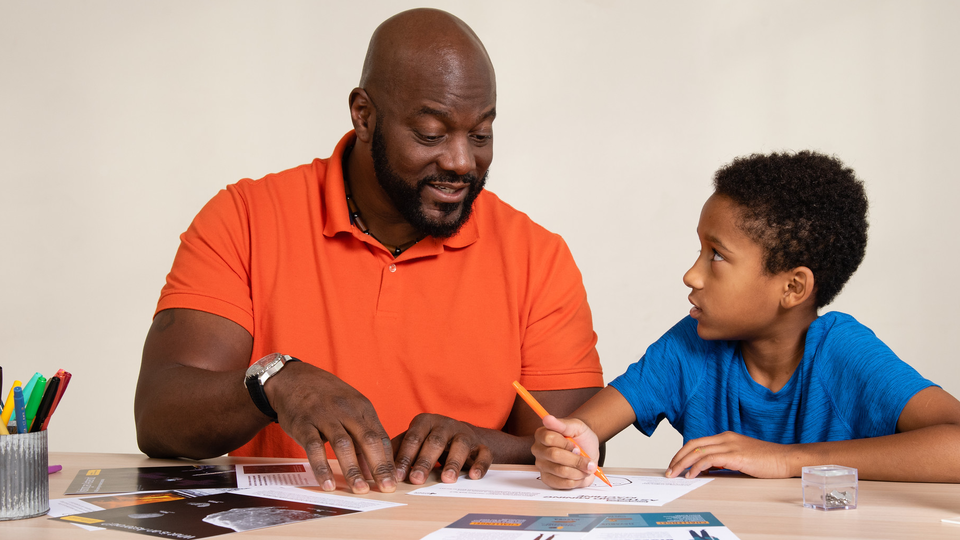 An adult and child working together on a science activity kit. 