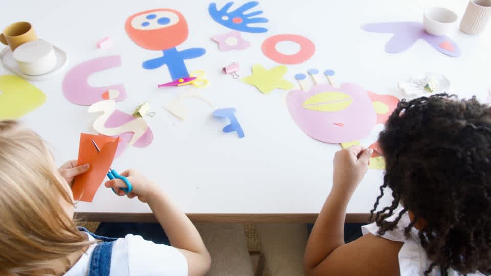 two children cutting out shapes using colorful cardboard paper 