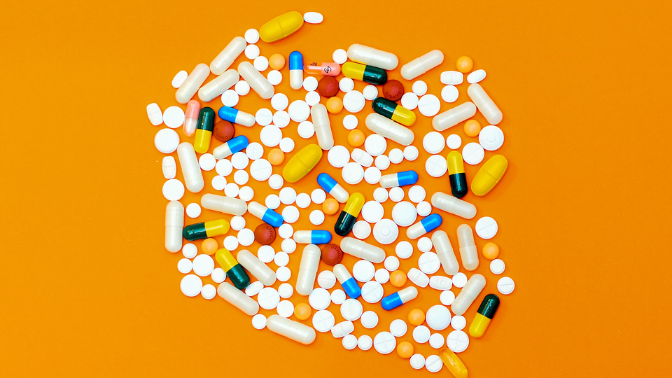 A combination of pills in different sizes and backgrounds on top of an orange background. 