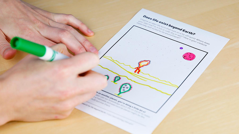 Close-up photo of a person drawing aliens on a worksheet with a marker