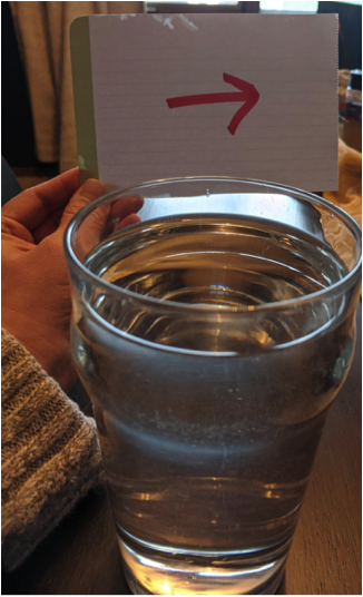 A glass of water in front of a piece of paper with an arrow pointing to the viewer's right 
