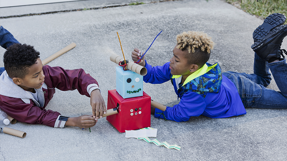 Two children playing with a makeshift cardboard robot 