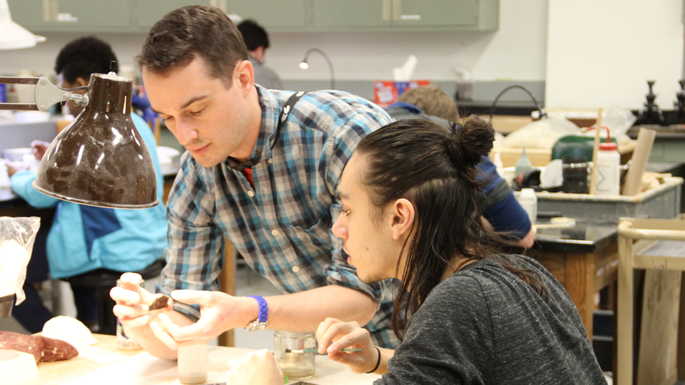 Paleontologist Dr. Alex Hastings shows a younger person a fossil. 