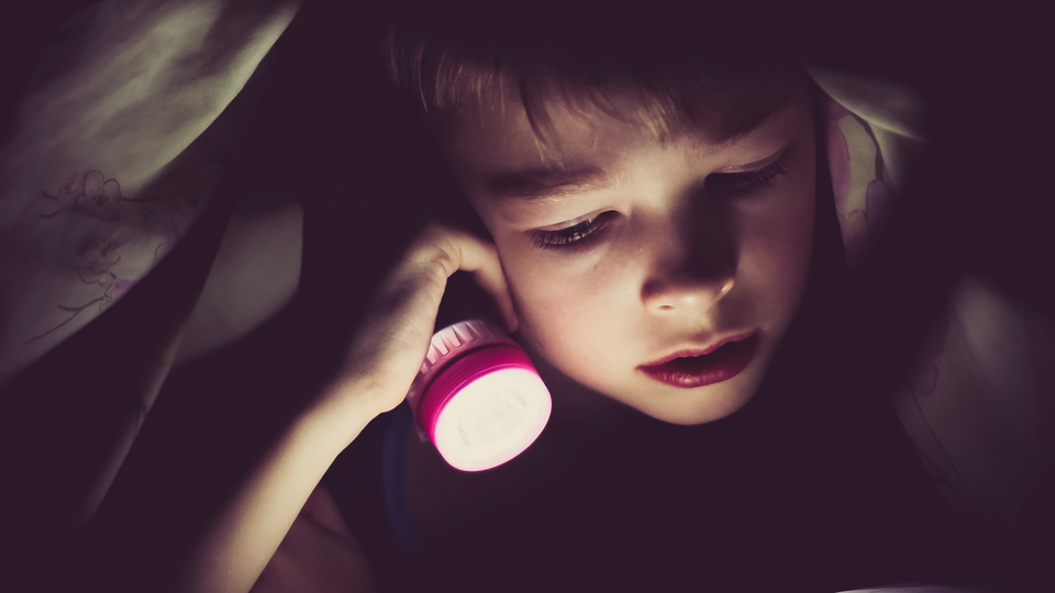 Child holding a flashlight under a blanket 