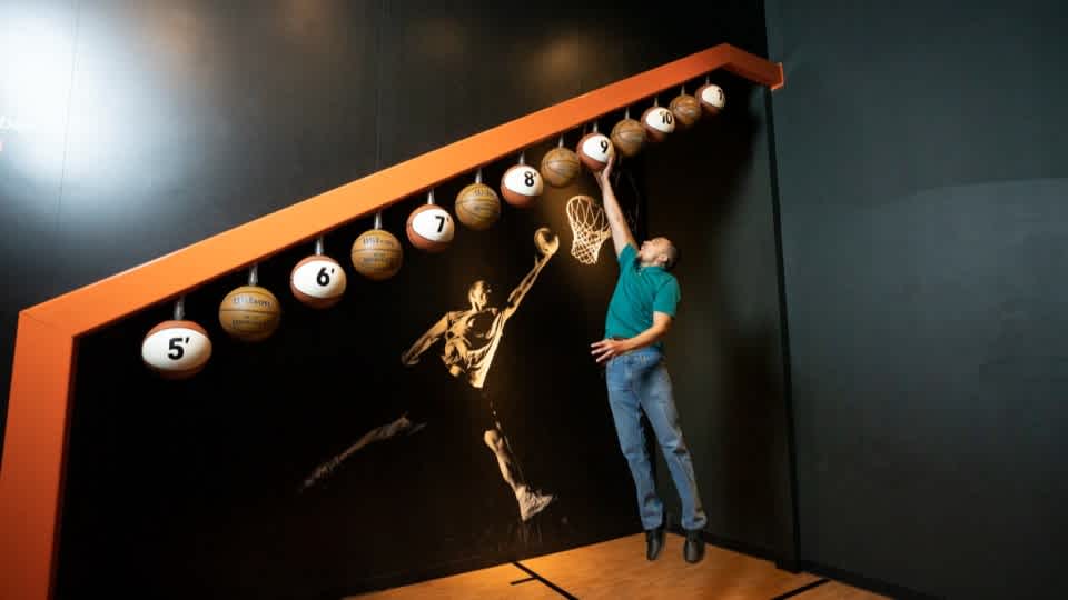 Person jumping to touch one of the basketballs in the Sportsology exhibit. 