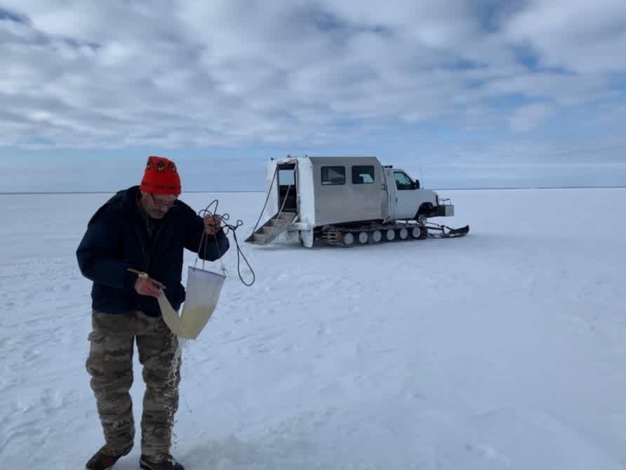 Researcher Mark Edlund standing on a frozen lake, checking to see how the algae are coming along in early March of 2019.