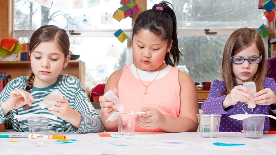Three kids gluing paper to plastic cups.