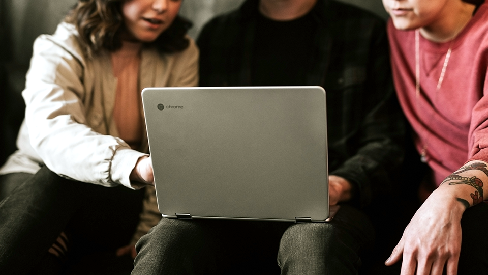 Three people gesturing toward a Chromebook laptop