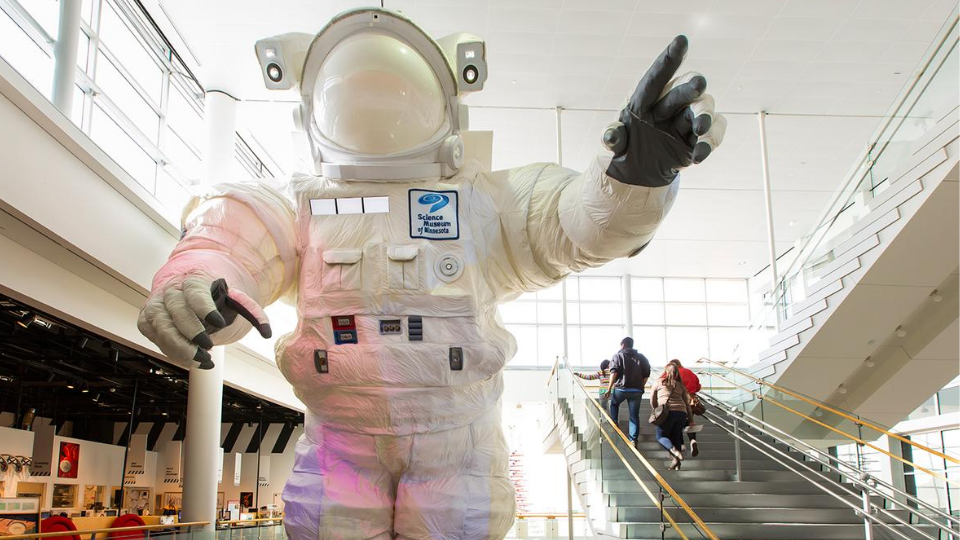 Image of the giant astronaut at the Science Museum with a family walking up the stairs nearby