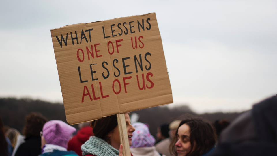 Cardboard sign reading "what lessens one of us lessens all of us." 