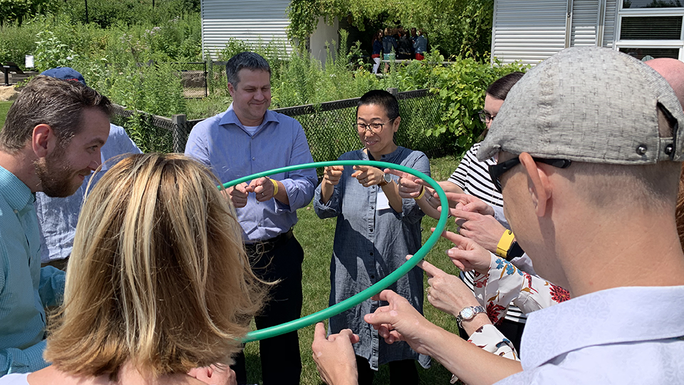 Work group balancing a hula hoop on their fingers 