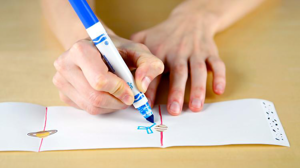 Close-up image of a person drawing a space probe on a piece of paper with a marker