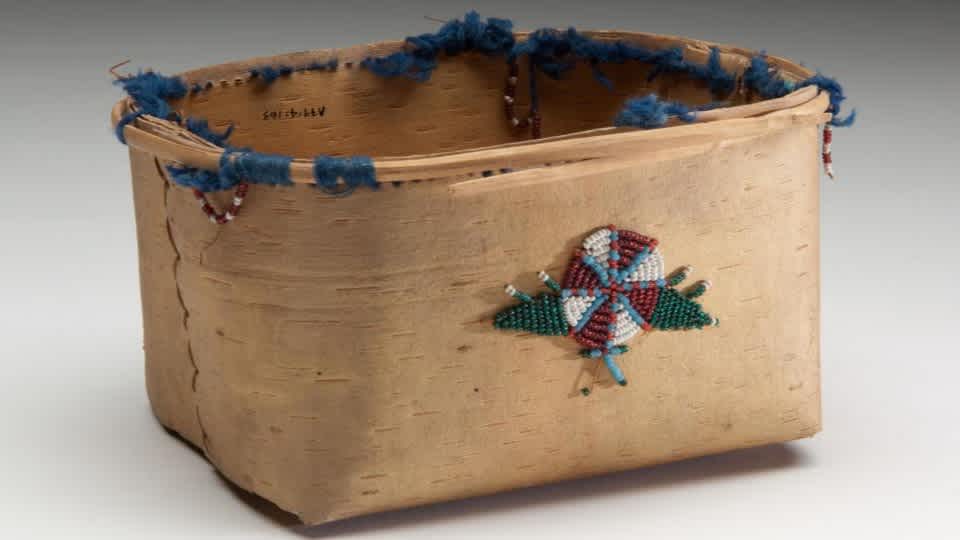 Basket, birchbark with rectangular opening and bottom. Remnants of red and white beaded loops and blue yarn around rim. glass beadwork on one side of a red and white circle with blue lines and green triangles.