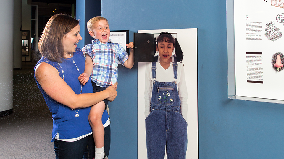 A mom holds a child while looking in the Human Body Gallery. 