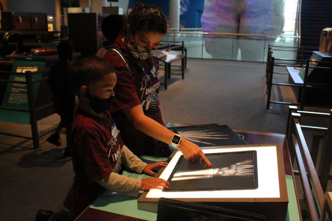 A photo of a child and their guardian pointing to a printed x-ray of a human hand. 