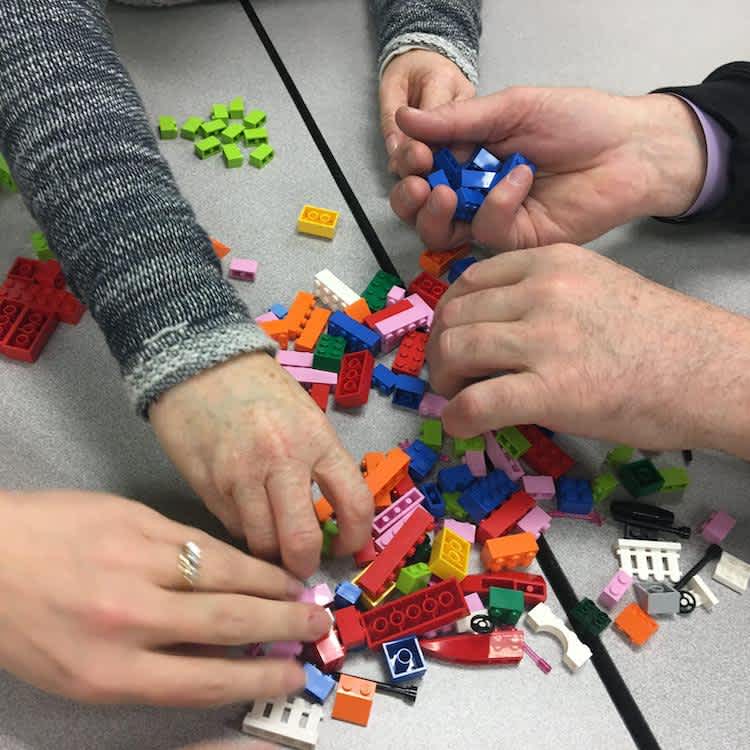 Photo of multiple hands putting LEGO together. 